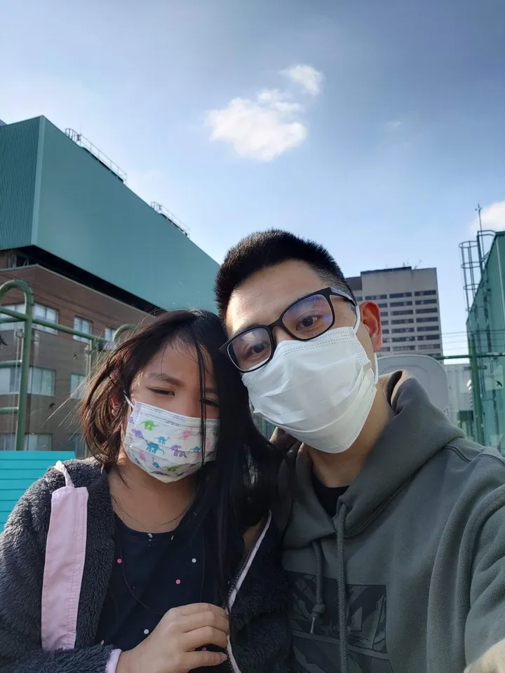 A selfie of me and my daughter, both in face masks, outside under a blue sky.